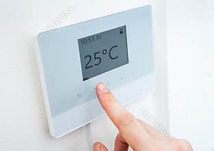 Heating concept. Hand is adjusting temperature in room on digital thermostat control.