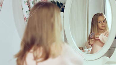 Fashionable little lady combing her hair and looking in the mirror