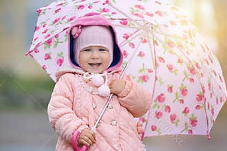 Joyful child with pink flower umbrella in the sun light after rain