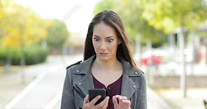 Perplexed woman checking phone looks at camera