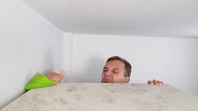 Home cleaning concept. a man wipes dust from a high cabinet in his house