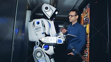Male specialist is explaining to a cyborg what to do with plugged-in servers