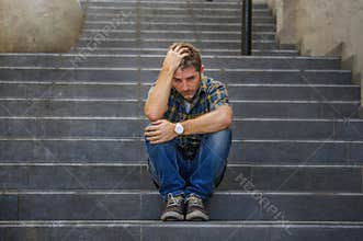 Young sad and desperate man sitting outdoors at street stairs suffering anxiety and depression feeling miserable crying in