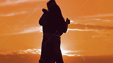 Silhouette man and girl of a happy young married couple slow dancing outside at sunset. Couple enjoying on nature the