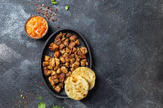 COLOMBIAN FOOD. Fried pork CHICHARRON, AREPAS and colombian tomato sauce. Top view. Black background