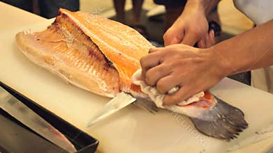 Close-up of sushi chef show one`s capability slices fresh salmon at sushi bar.