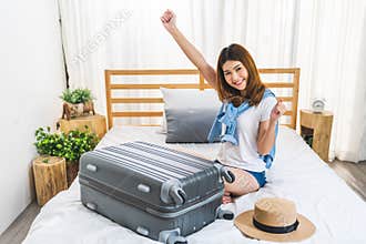Young cute happy Asian girl finished packing suitcase luggage on bed in bedroom, ready to go abroad solo trip