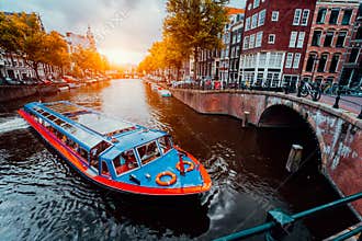 Tour boat at famous Dutch canal on sunset evening. Traditional Dutch bridges and medieval houses. Amsterdam Holland