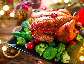 Christmas family dinner. Roasted chicken on holiday served table, decorated with gifts and burning candles. Roasted turkey