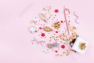 Gift or present box with confetti stars, golden ribbon and holiday decoration on pastel pink background. Christmas flat lay.