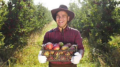 Portrait of happy farmer in hat standing at apple garden