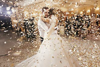 Gorgeous bride and stylish groom dancing under golden confetti a