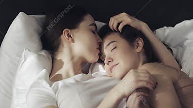 Lesbian couple embracing in the bed at home. One girl kisses another girl when she is sleeping Slow motion. Lifestyle