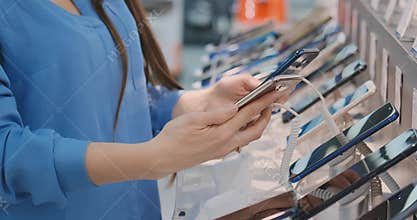 Closeup of woman`s hand choosing for buying a new smart phone near a shop window in an electronics store