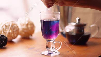 Woman squeezes a lemon into a of blue Thai tea. Blue tea reaction to lemon juice. Blue tea turns purple. Slow motion