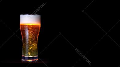 Glass of golden craft beer with white foam and moving bubbles isolated at black background