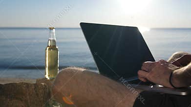 Male hands typing text on modern laptop on beach