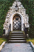 Antique arched wrought-iron doors in an old stone fortress wall using green lush ivy. Beautiful antique frnar over the old door