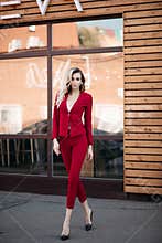 Pretty elegance stylish lady in red suit and black shoes posing at camera.