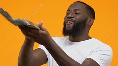 Happy young male throwing dollars around wasting money, luxury lifestyle, wealth