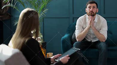 Man client sitting with female psychologist on the comfortable couch during the psychological session at the blue office