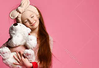Smiling baby girl holding a white teddy bear in the room a pink backdrop.