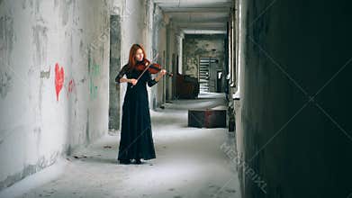 Violinist plays instrument in an empty hallway of abandoned building.