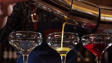 Bartender hands pouring three colored cocktails simultaneously - close up