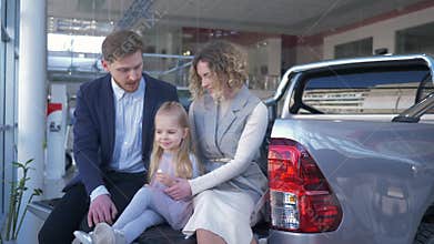 Auto salon, young family with child chooses vehicle and communicate with each other while sitting in trunk at car