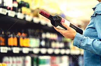 Alcohol shelf in liquor store or supermarket. Woman buying a bottle of red wine and looking at alcoholic drinks in shop.
