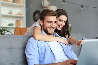Young couple doing some online shopping at home, using a laptop on the sofa.