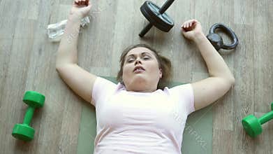 Fat woman lying exhausted on floor in fitness club