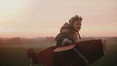 Happy little pilot boy starts to run in fun cardboard plane on sunset autumn field, playing and having fun slow motion.