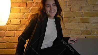 Portrait of young caucasian girl with wavy hair sitting on sofa and watching the TV with great enthusiasm on cosy home