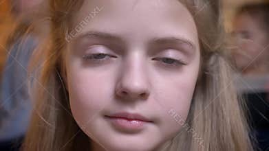 Close-up portrait of small pretty caucasian girl smiling modestly into camera in cosy home atmosphere.