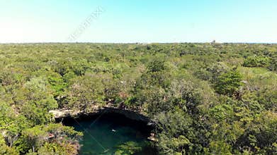 An overhead shot of the jungle and the El Jardin del Eden cenote filled with swimmers.