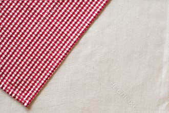 Red and White Checked Cloth at angle on upper corner of off white or cream colored linen table cloth. Horizontal above view with