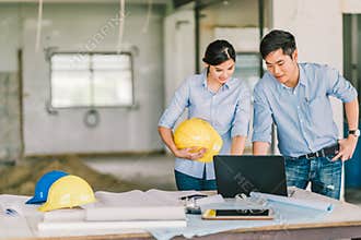 Young Asian engineer couple work together using notebook computer at building construction site. Civil engineering meeting concept