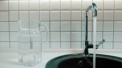 Man opens tap and flow of water pours into sink indoors.