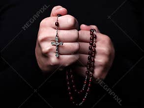 Female hands praying holding a rosary with Jesus Christ in the cross or Crucifix on black background.