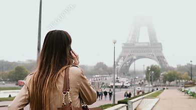 Young happy woman walking in downtown of Paris, France near the Eiffel tower and talking on mobile phone.
