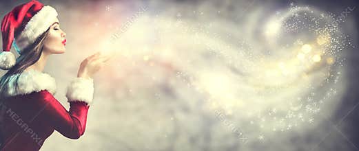 Christmas scene. Beauty brunette young woman in santa party costume blowing snow