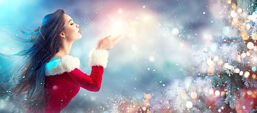 Christmas scene. Santa. Brunette young woman in party costume blowing snow