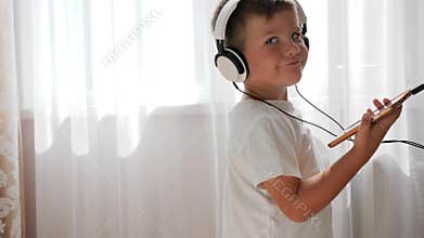 Smiling kid with phone into hands listening to music across headset and dancing in room
