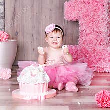 1 year baby girl in pink dress with her first birthday cake