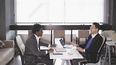 European man and African American man sitting in armchairs and negotiate