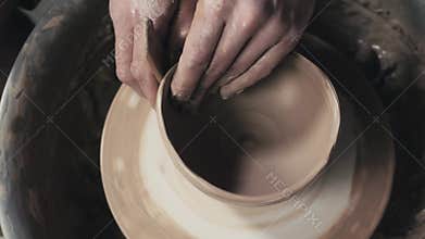 Potter shapes the clay product with pottery tools on the potter`s wheel, top view, toned cinematic, craft factory