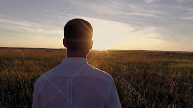 A young guy is walking on the field at sunset