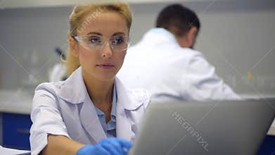 Smart female scientist in safety glasses typing on computer
