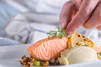 Chef in hotel or restaurant kitchen cooking, only hands. Prepared salmon steak with dill decoration